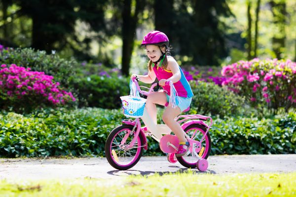 دوچرخه سواری کودکان بچه در دوچرخه در پارک آفتابی دختر کوچولو با لذت بردن از دوچرخه سواری در راه خود را به مدرسه در روز گرم تابستان کودک پیش دبستانی یادگیری برای تعادل در دوچرخه در کلاه ایمن ورزش برای بچه ها