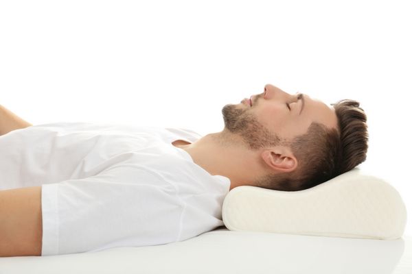 مرد جوان خوابیدن در رختخواب با بالش ارتوپدی در برابر زمینه سفید مفهوم منظر سالم