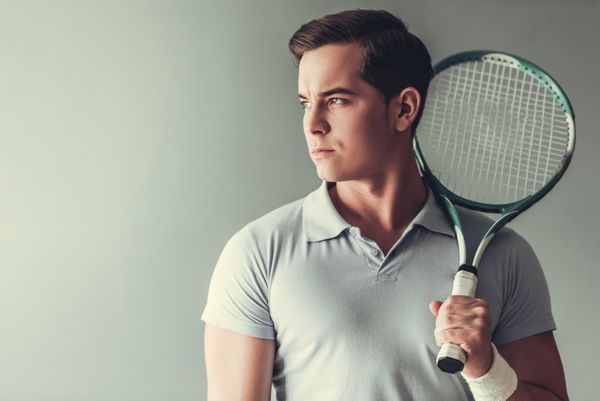 مرد جوان ورزش بازیکن تنیس جذاب در پس زمینه خاکستری