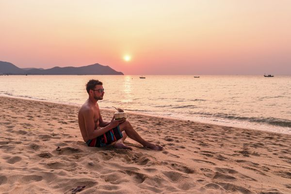 پرتره خود غروب خورشید در ساحل توسط اقیانوس با آسمان مشتاق مرد جوان در ساحل با نارگیل نوشیدنی در هنگام غروب آفتاب مرد مسافر شاد پاتایا تایلند Bangsaray