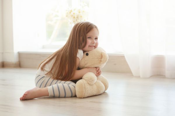 دختر کوچک ناز در حالی که نشسته روی زمین در آغوش خرس عروسکی می کشد