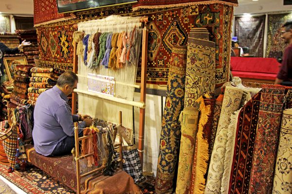 اصفهان اکتبر 2016 کارکنان خدمات مشتری با استفاده از یک فرش ایرانی باستانی در فروشگاه سنتی در بازار بزرگ اصفهان ایران فرش های مقرون به صرفه برای خرید پول بسیار ارزشمند هستند