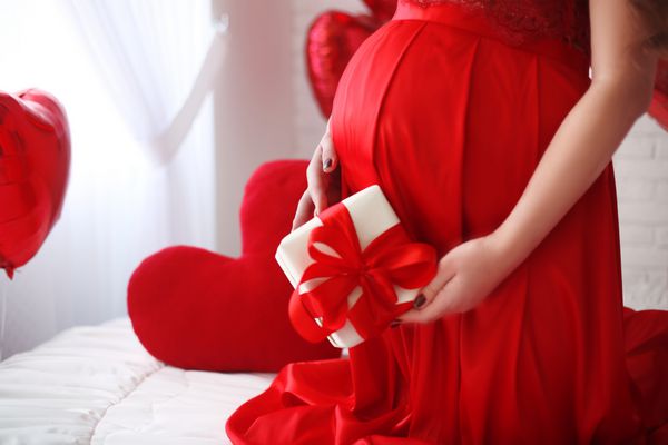 شکم یک زن باردار با جعبه هدیه بیش از قرمز است مادر و حاملگی Tummy بیش از هدیه ولنتاین بالن قلب جدا شده بر روی زمینه سفید