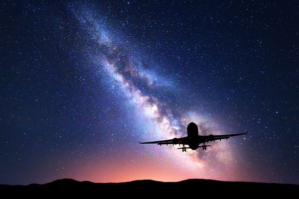 راه شیری و شبح یک هواپیما چشم انداز با هواپیما مسافری در آسمان پر ستاره در شب پرواز می کند پس زمینه فضایی هواپیما فرود در پس زمینه شیری رنگارنگ هواپیما