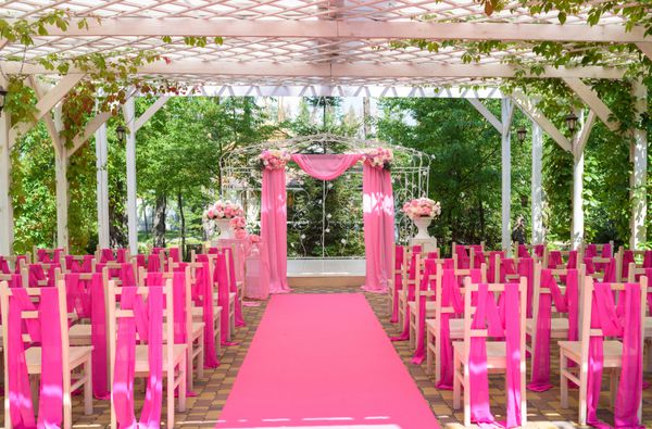 محل مراسم عروسی در رنگ صورتی با کاخ عروسی تزئین شده با گل و پارچه صورتی و صندلی های چوبی برای مهمانان در هر طرف خارج از منزل آرایش عروسی زیبا با صندلی در هر طرف