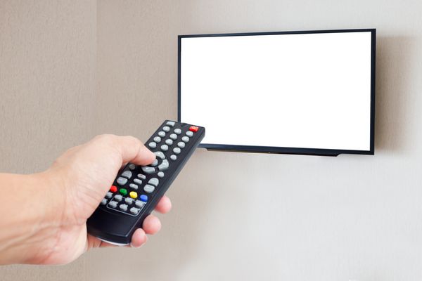 دست نگه داشتن کنترل از راه دور با تلویزیون صفحه خالی روی دیوار