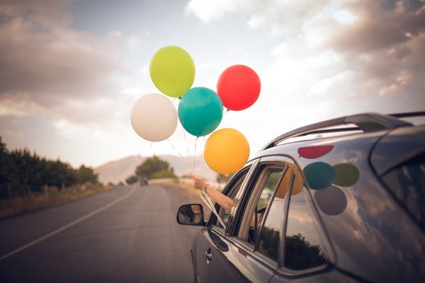 دختر بالن های رنگی را از پنجره اتومبیل می گیرد آزادی شادی سفر جاده ای و مفهوم جشن