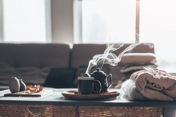 جزئیات عمر زندگی در داخل خانه اتاق نشیمن ژاکت و فنجان چای با بخار در سینی خدمت در میز قهوه صبحانه بیش از مبل در نور خورشید صبح مفهوم پاییز یا زمستان مناسب است