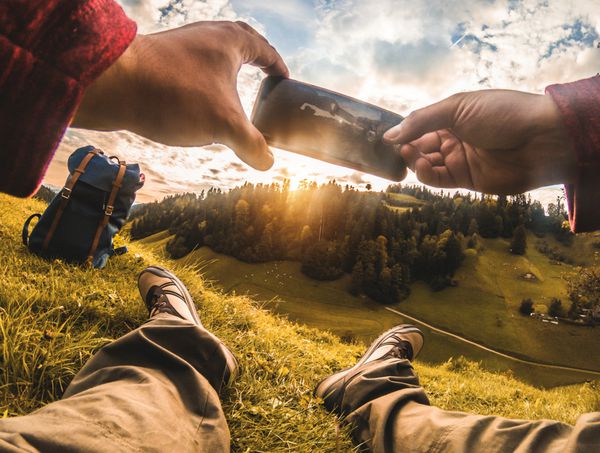 کوهنورد جوان با گرفتن عکس از غروب خورشید زیبا با گوشی هوشمند در طی روزهای تعطیل Hiker لذت بردن در کوه ها در فصل پاییز مفهوم سبک زندگی و فناوری سالم تمرکز بر روی کفش