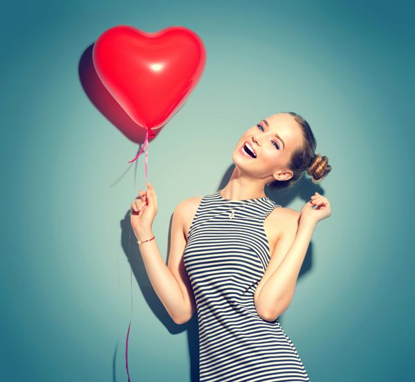 Beauty girl with red heart shaped air balloon laughing over green background Beautiful Happy woman on birthday party Love Valentine