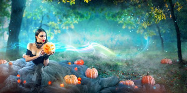 جادوگر هالووین با کدو تنبل و چراغ سحر و جادو در یک جنگل تاریک زن زیبا زن شگفت زده در لباس جادوگر نگه داشتن کدو تنبل طراحی گسترده هنری حزب هالووین
