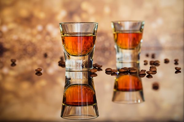 کنیاک یا لیکور و دانه های قهوه در یک میز شیشه ای مفهوم تعطیلات فصلی