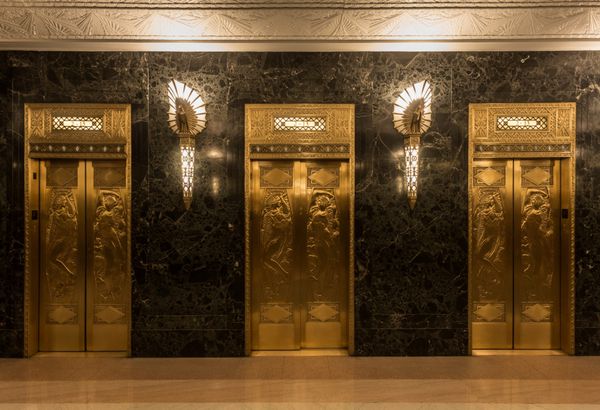 آسانسور طلایی با مجسمه های امدادی و دیوار سنگ مرمر با چراغ