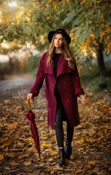 دختر زیبا در کلاه فرفری و کلاه سیاه در کنار برگ های پاییز رنگارنگ با چتر ایستاده است کار هنری زن رمانتیک مدل تندرستی ملایم در زیر باران به دنبال دور