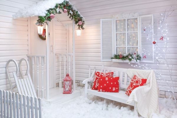 بیرونی زمستانی یک خانه ای با دکوراسیون کریسمس در سبک آمریکایی حیاط تحت پوشش برف با حیاط درخت نیمکت سفید و سورتمه های چوبی قدیمی