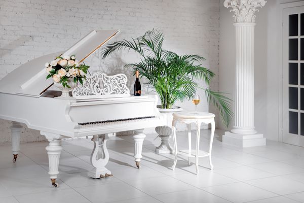 پیانو بزرگ در یک کلاسیک داخلی لوکس سفید با کف دست و گل