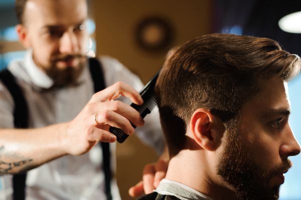 کارشناسی ارشد مو و ریش مردان در آرایشگاه را کاهش می دهد آرایشگری برای یک مرد جوان مدل مو را می سازد