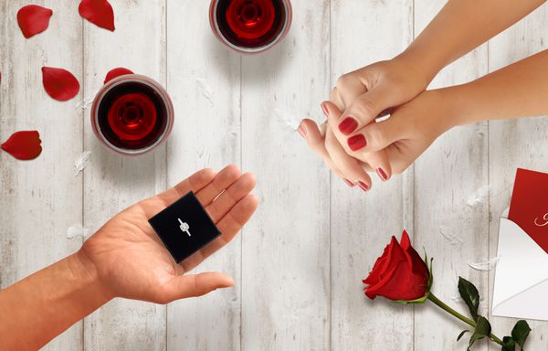 مردان دست حلقه نامزدی را به زن دست می دهد پیشنهاد عشق صحنه با لیوان گل رز پاکت روی میز چوبی