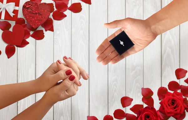 مردان دست هدیه با حلقه نامزدی را به زن دست می دهد پس زمینه رمانتیک با گلبرگ گل سرخ هدیه بر روی میز