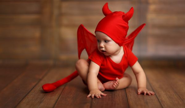کودک خنده دار در لباس هالووین شیطان در پس زمینه چوبی