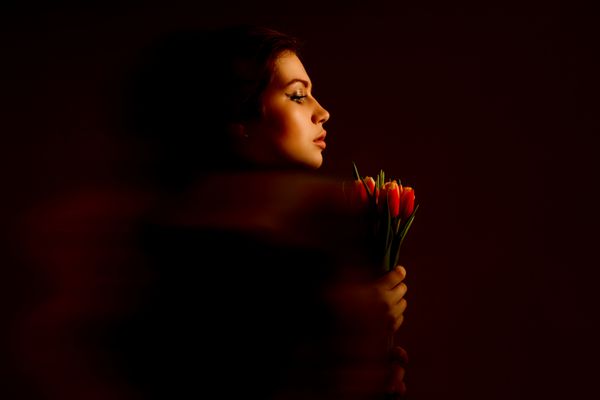 پرتره یک زن جوان با یک دسته گل لاله در یک پس زمینه تاریک