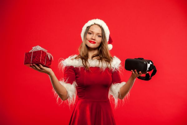 کریسمس X-mas زمستان مفهوم شادی سبیل زیبا جوان با موهای بلند در Santa کلاه زنانه پوشیدن رئوس مطالب واقعیت مجازی بر روی جعبه هدیه جعبه قرمز