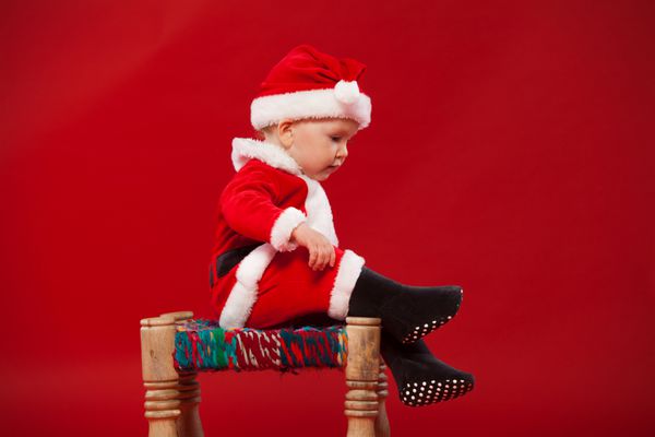 بچه ناز در لباس بابا نوئل نشسته روی صندلی