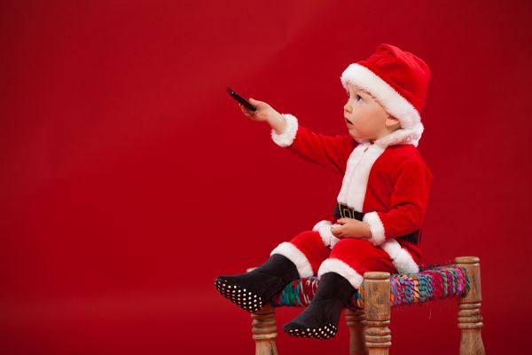 بچه ناز در لباس بابا نوئل نشسته روی صندلی تلفن