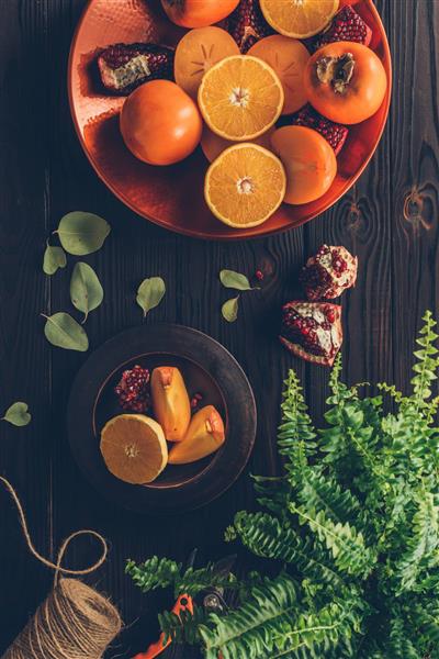 تصویر بالا از میز چوبی با برشی از پرتقال و انار