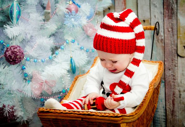 گریه و غمگین دختر بچه نشسته زیر یک درخت آبی در یک کلاه راه راه قرمز و سفید رنگ مفهوم یک سال جدید در یک کارت کریسمس