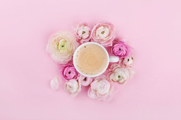 فنجان صبحانه قهوه و گل های زیبا در زمینه صورتی از بالا در سبک صاف