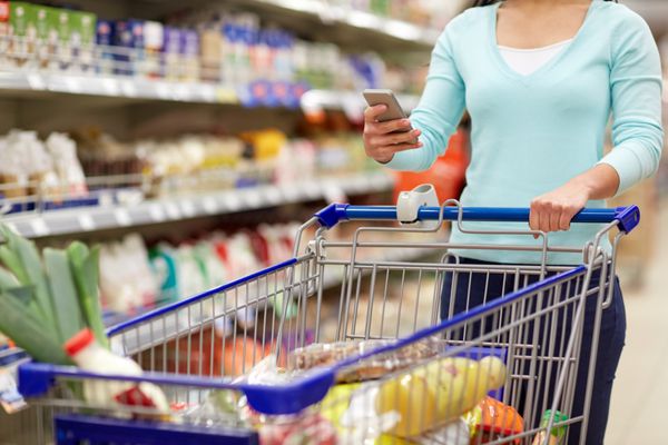 زن با گوشی هوشمند خرید مواد غذایی در سوپرمارکت