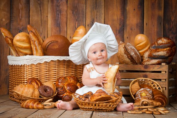 کودک کوچک یک کریسانت را در پس زمینه سبد ها با رول و نان آماده می کند
