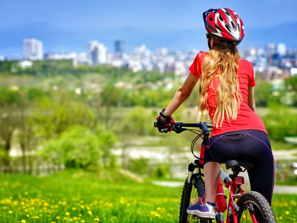 دوچرخه دختر استراحت دارد زن با پوشیدن کلاه ایمنی ورزشی سواری به شهر باز می گردد دوچرخه سواری برای سلامتی خوب است دوچرخه سوار به شهر در فاصله نگاه می کند