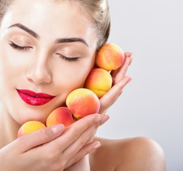 زن زیبا نگه داشتن یک زردآلو آبدار هلو پوست کامل ماسک صورت میوه آرایش حرفه ای
