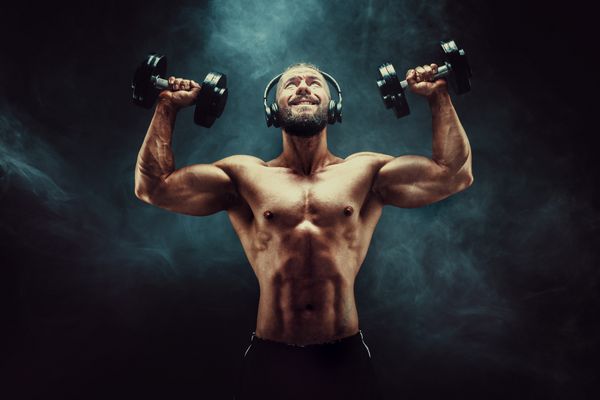عضلات ورزش مردانه با دمبل در استودیو در پس زمینه تاریک با دود بدنساز قوی با شش بسته کامل abs شانه دو سوکور سه پایه و سینه با هدفون