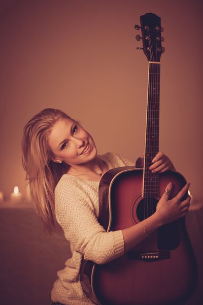 زن بلوند جوان بازی گیتار در نور شمع