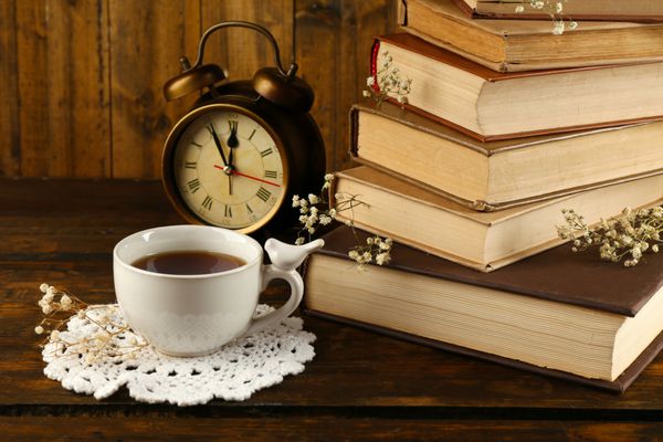 جام چای با کتاب و ساعت در زمینه های چوبی