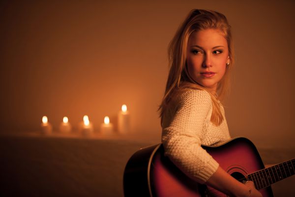 زن بلوند جوان بازی گیتار در نور شمع