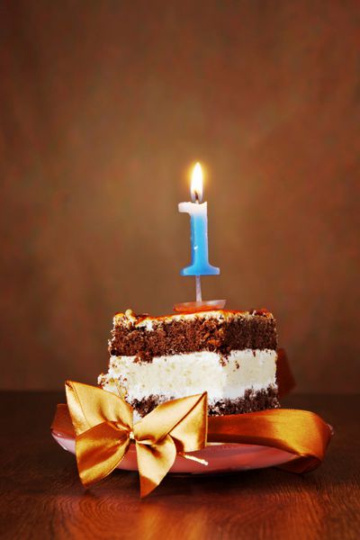 قطعه ای از کیک شکلاتی تولد با شمع بخار به عنوان شماره یک بر روی پس زمینه قهوه ای