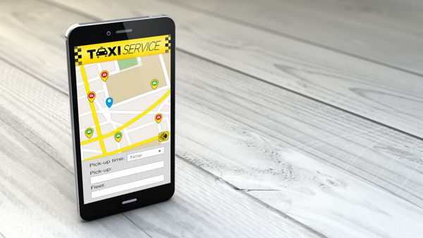 گوشی هوشمند با برنامه سرویس تاکسی بر روی جعبه سفید چوبی