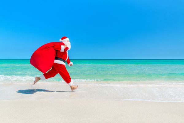 بابا نوئل در حال اجرا در امتداد ساحل با کیسه ای پر از هدایا