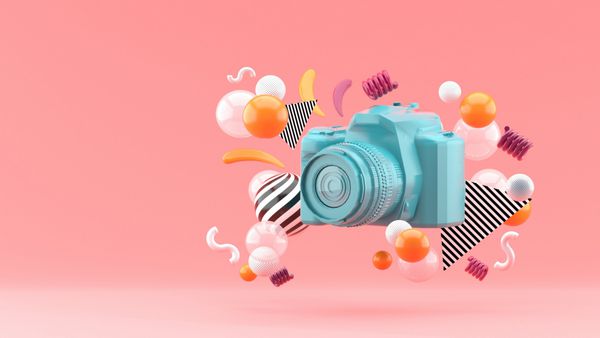 دوربین آبی توسط توپ های رنگارنگ در پس زمینه صورتی احاطه شده است 3D رندر