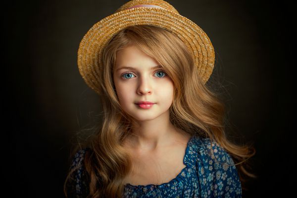پرتره یک دختر زیبا با چشم آبی در لباس پرنعمت و کلاه کودک با موهای درخشان براق در استودیو در پس زمینه تاریک