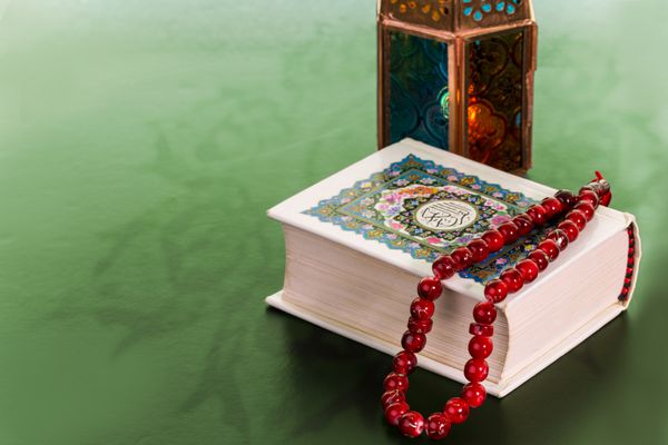 بستن کتاب مقدس قرآن و عید قرمز و یک فانوس روی زمینه سبز مفهوم رمضان کریم