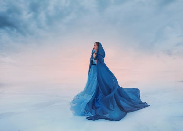 ملکه برفی در بارانی آبی است که در باد فرو می ریزد یک مسافر در پس زمینه طلوع یا غروب آفتاب و دره یخ زده با برف و ابرها پوشیده شده است جایی که آسمان به زمین می آید