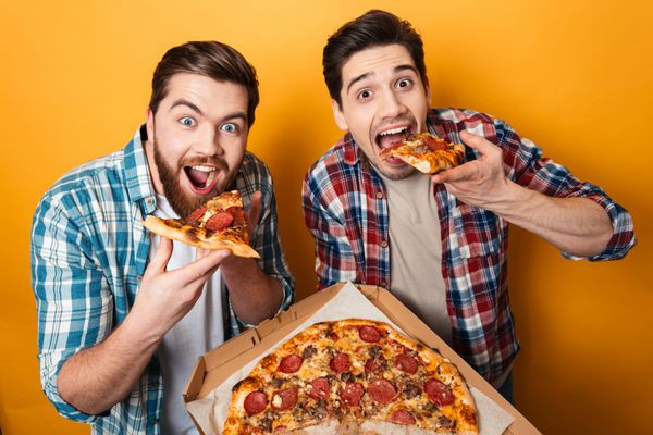 پرتره از دو مرد جوان گرسنه خوردن پیتزا جدا شده بر روی زمینه زرد