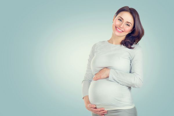 زن باردار شاد کردن شکمش پرتره مادر حامله در میانه سال نوازش شکم و لبخند بزنید مفهوم بارداری سالم زن باردار در پس زمینه آبی