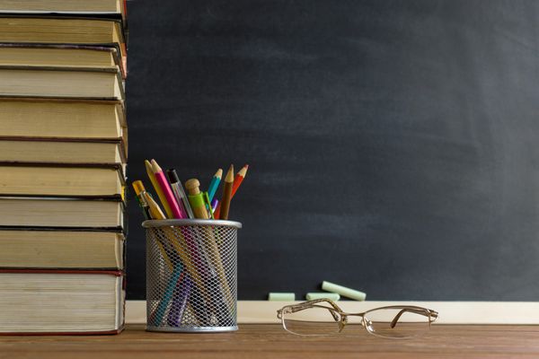 کتاب های معلم عینک و یک پایه با مداد روی میز در پشت یک تخته سیاه با گچ مفهوم روز معلم فضای کپی کنید