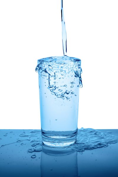 بیش از حد آب معدنی در شیشه ای شفاف با قطره و حباب جدا شده بر روی زمینه سفید پس زمینه آبی نزدیک است